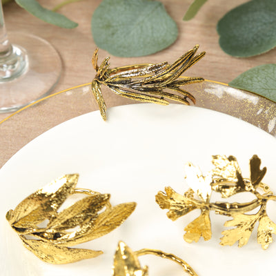 Gold leaf napkin rings on a white plate with greenery in the background.