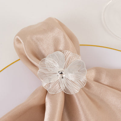 Silver flower napkin holder on a satin cloth atop a white plate.