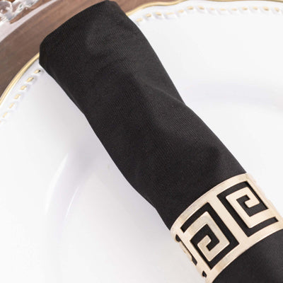 Black napkin holder with gold Greek key design on a white plate.