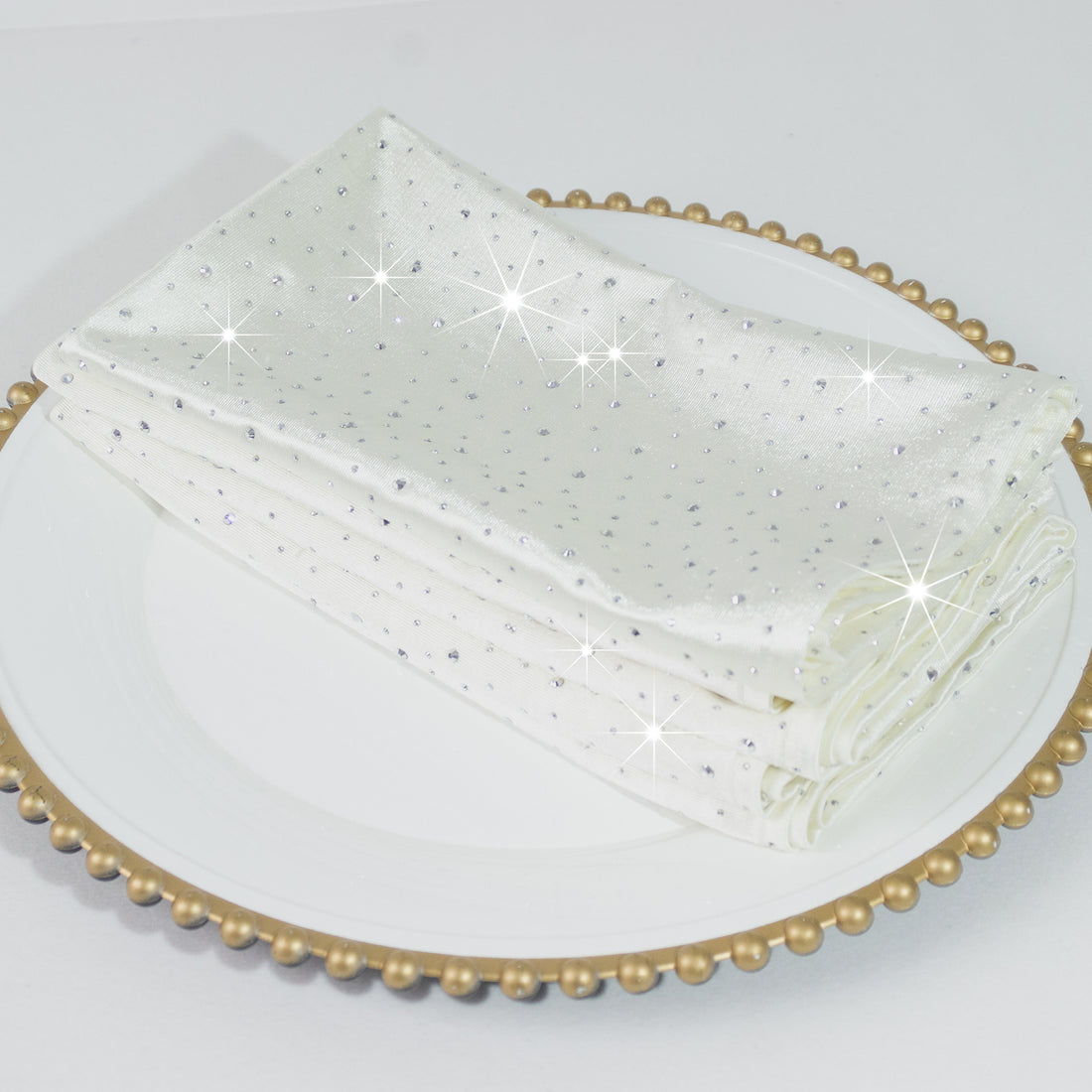 White napkins with sparkling embellishments on a decorative plate.