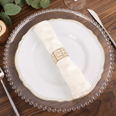 Elegant white plate with a gold-accented napkin and beaded charger on a wooden table.