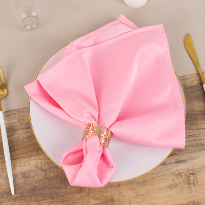 Pink satin napkin elegantly tied with a gold ring on a white plate.