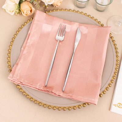 Pink satin napkin with silver fork and knife on a decorative plate.