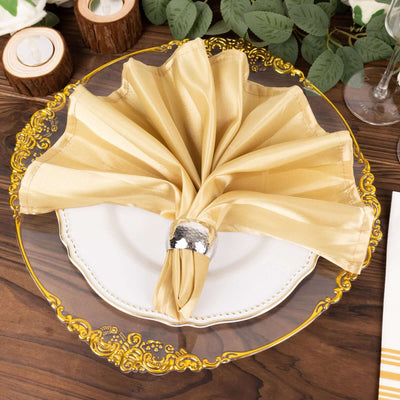 Elegant gold satin napkin arranged on a decorative plate with a silver napkin ring.