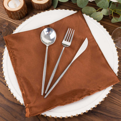 Elegant brown napkin with silver cutlery on a decorative plate.
