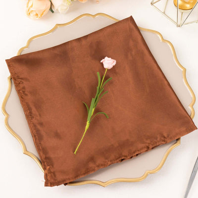 Brown satin napkin with a pink flower on a decorative plate.