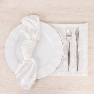 Elegant white plate with napkin and silver cutlery on a wooden table.