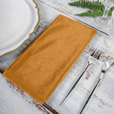 Orange cloth napkin on a rustic table setting with silverware.