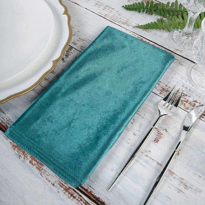 Teal fabric napkin on a rustic table setting with plate and cutlery.