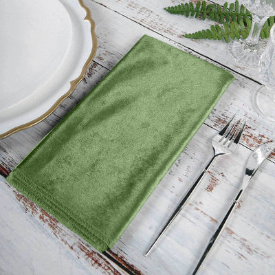 Green velvet napkin on a rustic table setting with cutlery and plate.