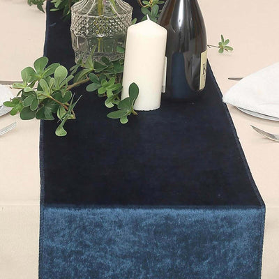 Navy velvet table runner with greenery and candle on a dining table.