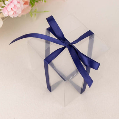 Clear gift box with a navy blue ribbon on a neutral background.