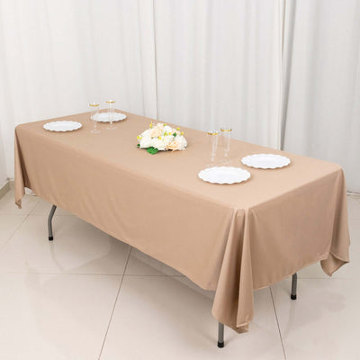 Beige tablecloth draped over a table set for an event with plates and floral centerpiece.