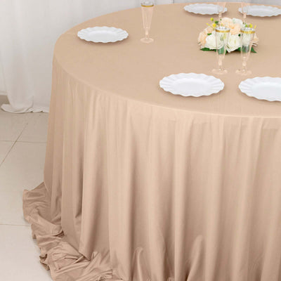 Beige round tablecloth draped elegantly over a table with white plates and floral centerpiece.
