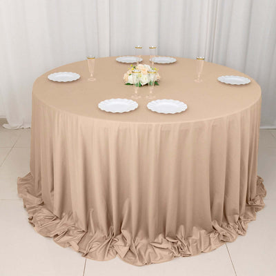 Round banquet table with beige tablecloth and white plates, elegantly set for dining.
