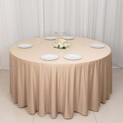 Round table with beige tablecloth, white plates, and floral centerpiece.