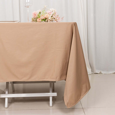 Beige tablecloth draped over a table with flowers in the background.