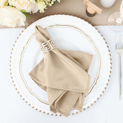 Elegant beige napkin with decorative ring on a white plate, styled for dining.