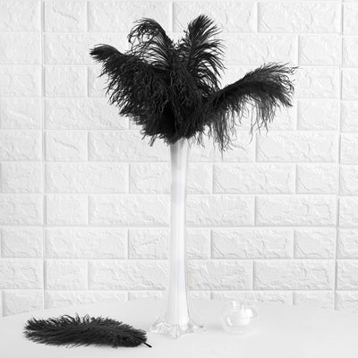Black feather arrangement in a white vase on a table.
