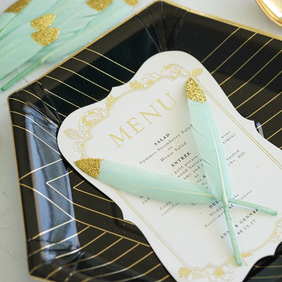 Elegant black and gold plate featuring a menu card and decorative feathers.