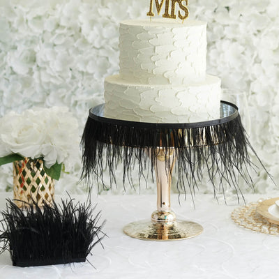 Elegant wedding cake with black fringe and decorative stand against floral backdrop.