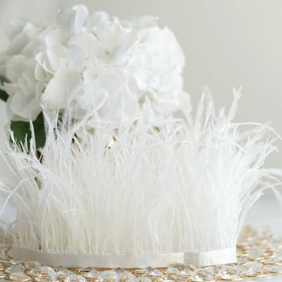 White decorative feathers with a floral arrangement in the background.