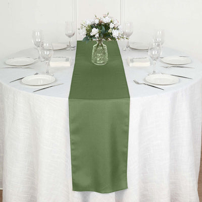 Green table runner on a white table set with glassware and flowers.