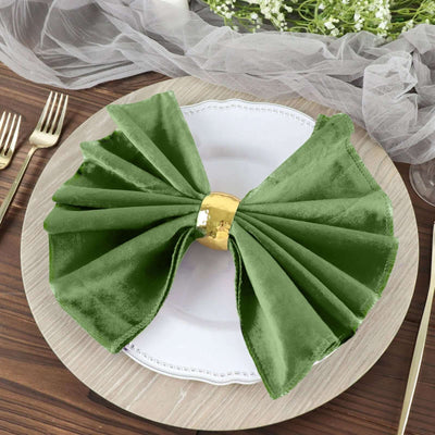 Green velvet napkin with gold ring on a plate, styled for elegant dining.