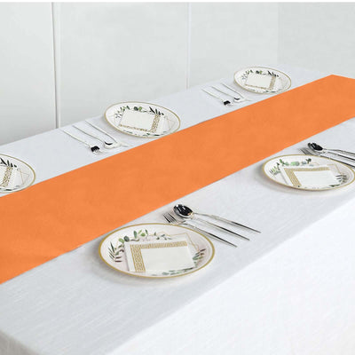 Orange table runner on a white table setting with decorative plates and cutlery.