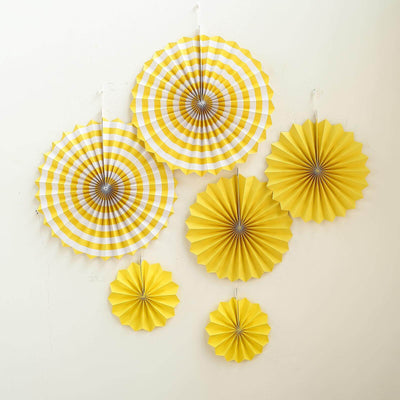Yellow decorative paper fans in various sizes hanging on a wall.