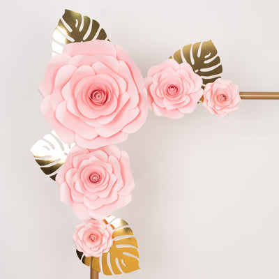 Pink paper roses with gold leaves on a white backdrop.