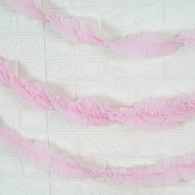 Pink ruffled garland on white textured wall.