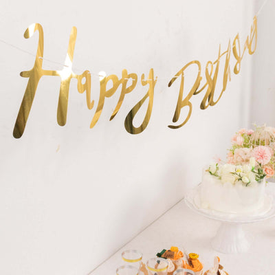 Gold "Happy Birthday" banner on a decorated table with cake and flowers.