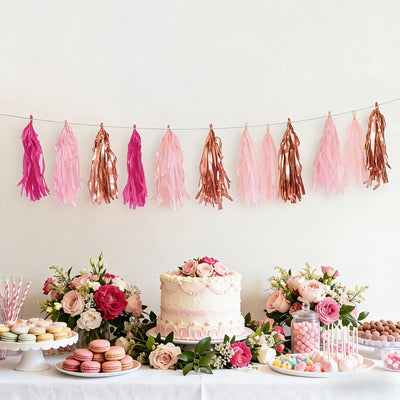Party decoration with pink and rose gold tassels above a cake and desserts display.