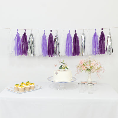 Purple and silver tassel garland with cake, cupcakes, and floral arrangement on table.