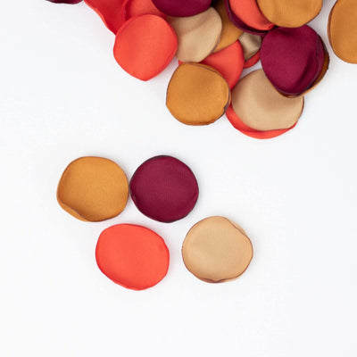 Colorful fabric circles in red, maroon, gold, and beige scattered on white background