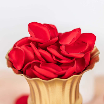 Red silk rose petals in a gold vase.