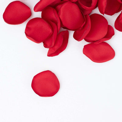 Red silk rose petals scattered on a white background.