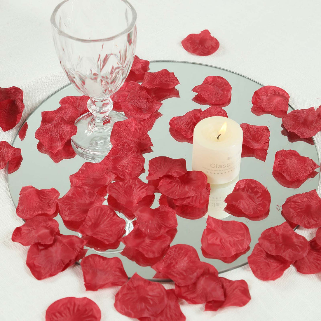 Romantic candle and wine glass on mirrored tray with red rose petals