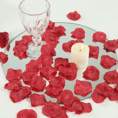 Romantic candle and wine glass on mirrored tray with red rose petals