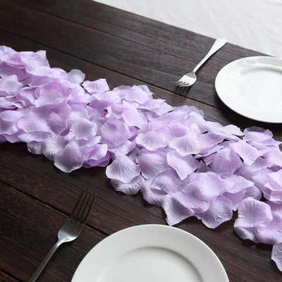 Purple silk flower petals arranged on a wooden table for decoration.