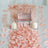 Pink rose petals with candles and a glass vase centerpiece on a white table.