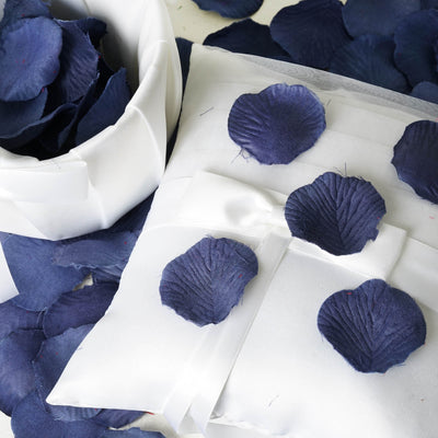 Navy blue silk rose petals on a white pillow and in a bowl.