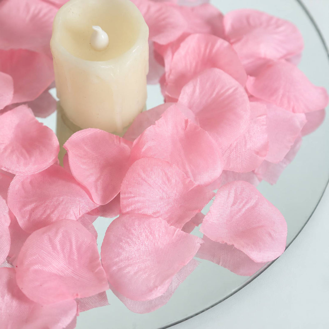 Pink rose petals surrounding a cream candle on a glass plate