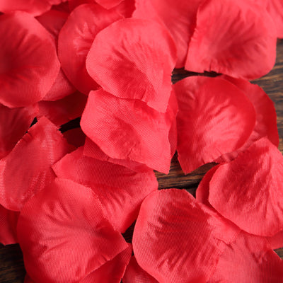Red silk rose petals scattered on a wooden surface.