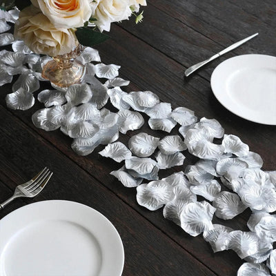 Elegant white petal table runner with roses, plates, and silverware on dark wood table.