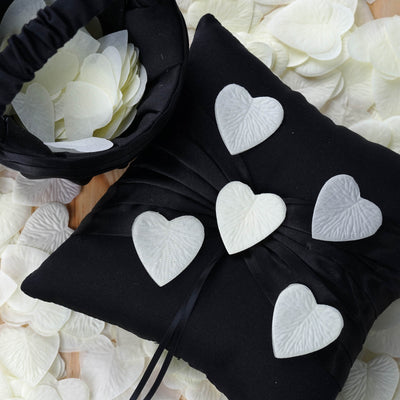 Black pillow adorned with white heart-shaped petals and a bowl of petals.