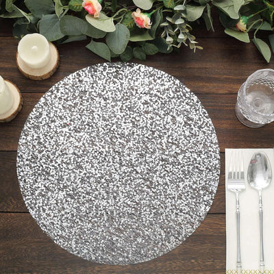 Silver glitter placemat on a wooden table with cutlery and candles.