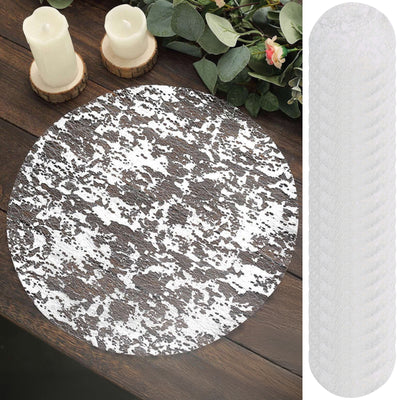 Round lace tablecloth in white and gray on a wooden table with candles and greenery.