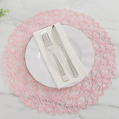 Pink woven placemat with white plate, silver cutlery, and napkin on marble surface.